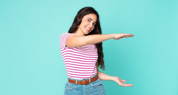 Young pretty woman smiling, feeling happy, positive and satisfied, holding or showing object or concept on copy space