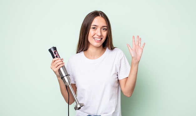 幸せに笑って、手を振って、あなたを歓迎し、挨拶する若いきれいな女性。ハンドミキサーのコンセプト