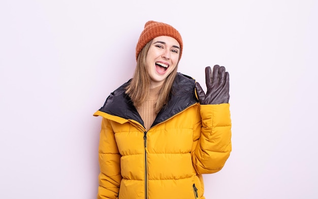 Young pretty woman smiling happily, waving hand, welcoming and greeting you. winter concept