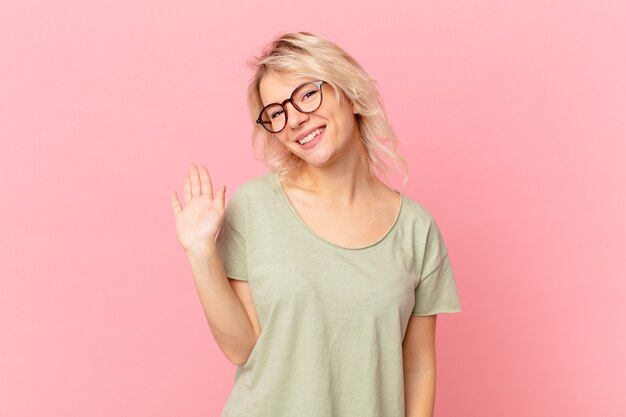 Young pretty woman smiling happily, waving hand, welcoming and greeting you