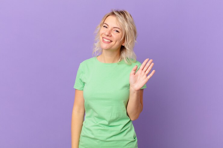 Photo young pretty woman smiling happily, waving hand, welcoming and greeting you