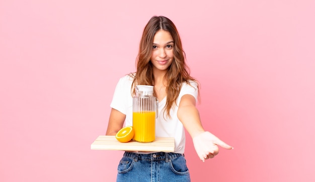 Young pretty woman smiling happily with friendly and  offering and showing a concept and holding a tray with an orange juice
