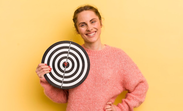 Young pretty woman smiling happily with a hand on hip and confident dart target concept