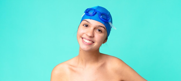 Молодая красивая женщина счастливо улыбается, положив руку на бедро и уверенная в плавательных очках