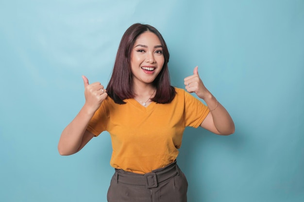 Young pretty woman smiling joyfully and looking happy feeling carefree and positive with both thumbs up isolated by blue background