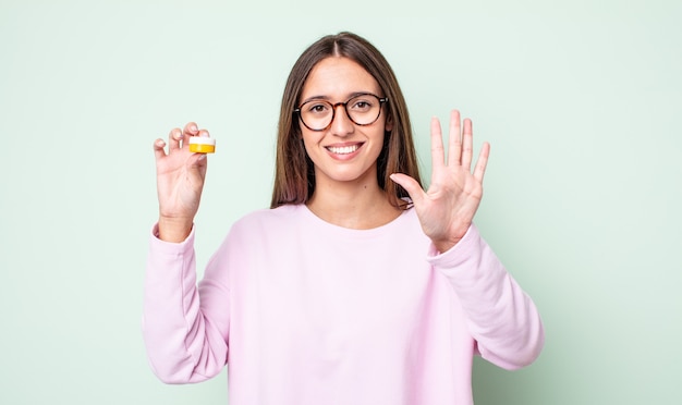 Young pretty woman smiling and looking friendly, showing number five. contact lenses concept