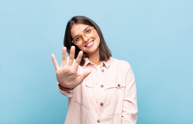 Young pretty woman smiling and looking friendly, showing number five or fifth with hand forward, counting down