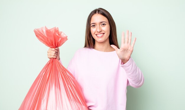 young pretty woman smiling and looking friendly, showing number five. trash concept