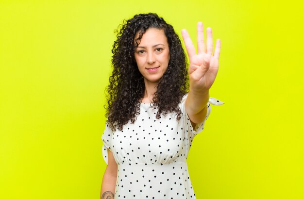 Foto giovane donna graziosa che sorride e che sembra amichevole, mostrando numero quattro o quarto con la mano in avanti, conto alla rovescia contro la parete di chiave dell'intensità