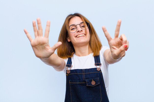 Young pretty woman smiling and looking friendly, showing number seven or seventh with hand forward, counting down against blue background