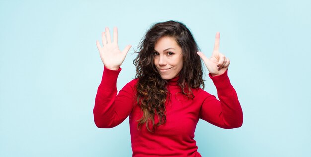 Foto giovane donna graziosa che sorride e che sembra amichevole, mostrando numero sette o settimo con la mano in avanti, conto alla rovescia sulla parete blu