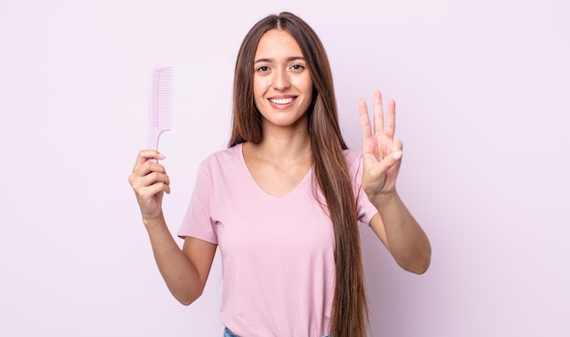 Young pretty woman smiling and looking friendly, showing number three. hair comb concept
