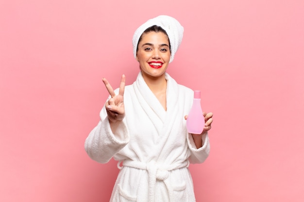 Young pretty woman smiling and looking friendly, showing number two or second with hand forward, counting down. bathrobe and face cleaning concept