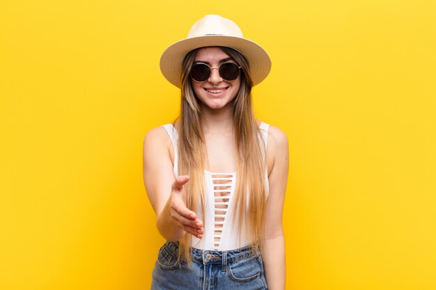 Young pretty woman smiling, looking happy, confident and friendly, offering a handshake to close a deal, cooperating