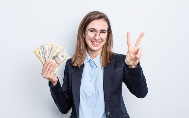 Young pretty woman smiling and looking happy, gesturing victory or peace. dollar banknotes concept