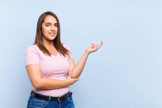 Young pretty woman smiling proudly and confidently, feeling happy and satisfied and showing a concept on copy space against blue wall