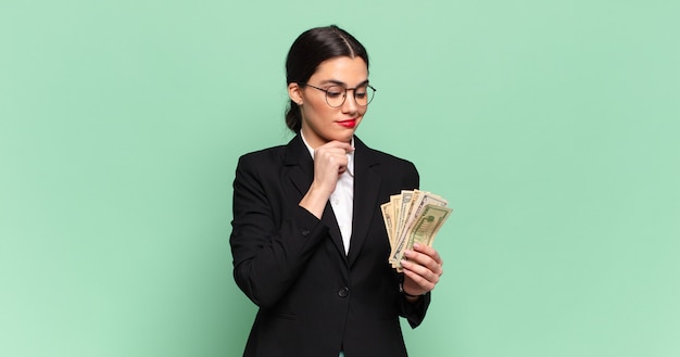 Young pretty woman smiling with a happy, confident expression with hand on chin, wondering and looking to the side. business and banknotes concept