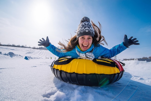 Young pretty woman at snow tubing rise hands up. slide from snow hill. winter activity