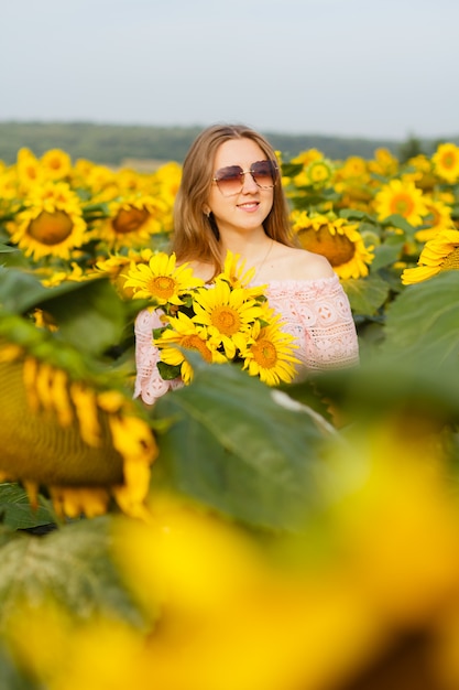 Young pretty woman stands among blooming sunflowers