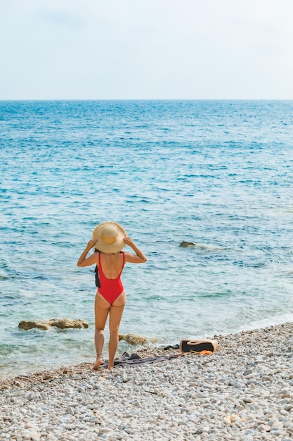 海のビーチで麦わら帽子の若いきれいな女性夏休み赤い水着