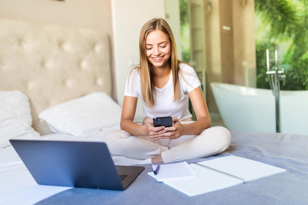 Giovane bella donna che studia con il portatile sul letto