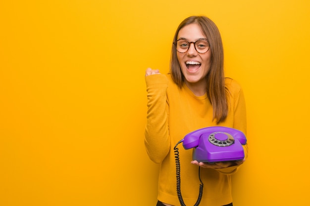 Young pretty woman surprised and shocked she is holding a vintage telephone
