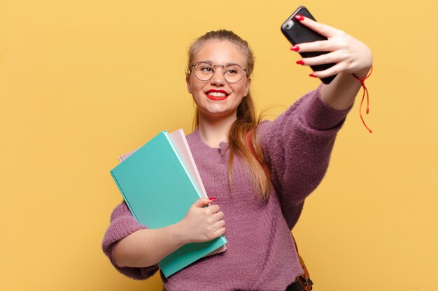 本を持っている間スマートフォンでselfie写真を撮る若いきれいな女性