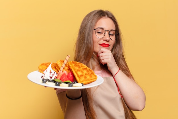 お菓子を皿に抱えて表情を考えたり疑ったりする若いきれいな女性