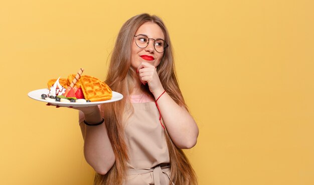 Foto giovane bella donna che pensa e tiene in mano un piatto con cialde