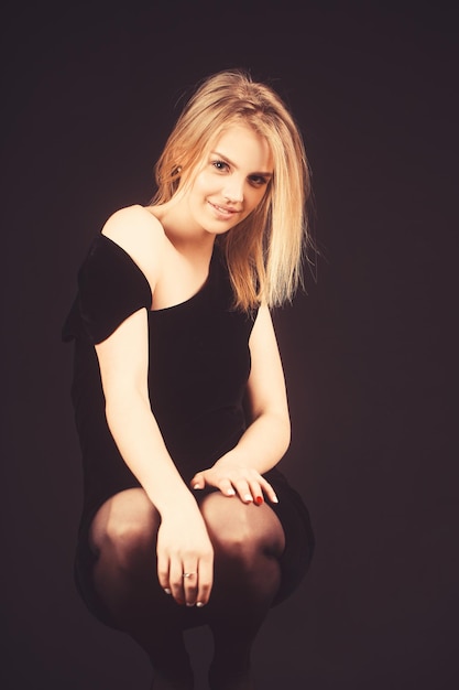 Young pretty woman in tight black dress posing on dark background