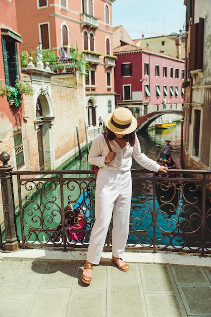 Фото Молодая красивая женщина-путешественница, стоящая на венецианском мосту, пересекает гондолы канала в воде