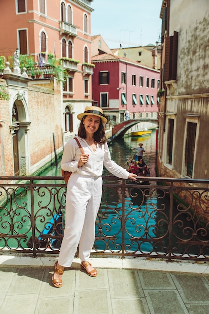 Young pretty woman traveler standing at venice bridge cross canal gondolas in water