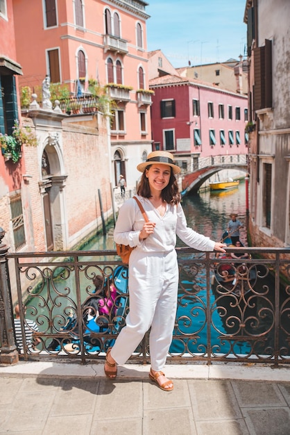 Young pretty woman traveler standing at venice bridge cross canal gondolas in water