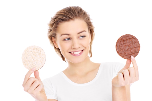 a young pretty woman trying to decide between a healthy and unhealthy cookie over white background