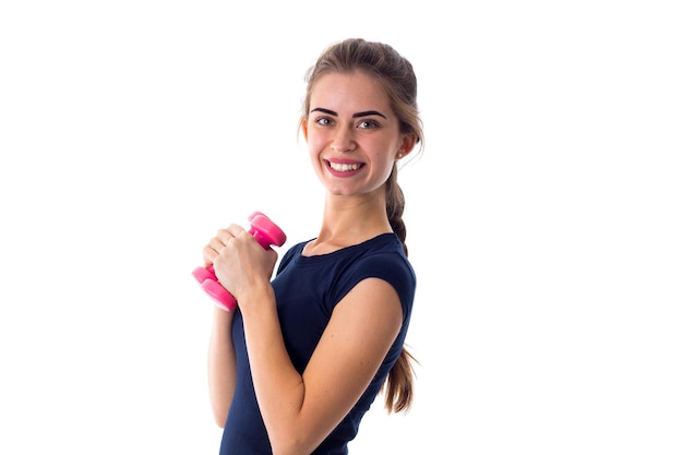 Young pretty woman in Tshirt holding pink dumbbells in front of her on white background in studio