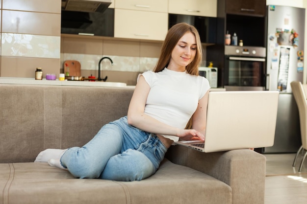 젊은 예쁜 여자는 거실에 소파에 앉아있는 동안 노트북을 사용합니다