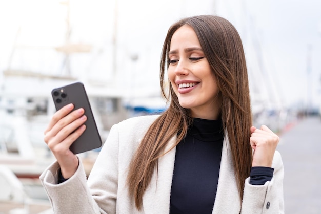 Young pretty woman using mobile phone at outdoors celebrating a victory