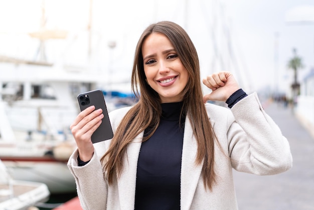 Young pretty woman using mobile phone at outdoors proud and selfsatisfied