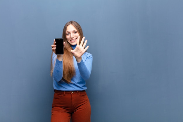 Young pretty woman using a smart phone against blue wall with a copy space