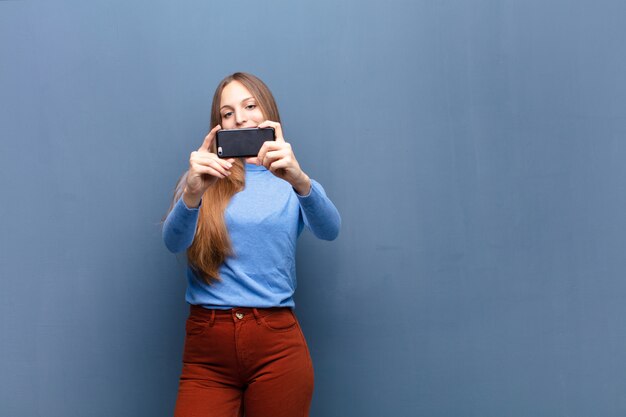 Young pretty woman using a smart phone against blue wall 