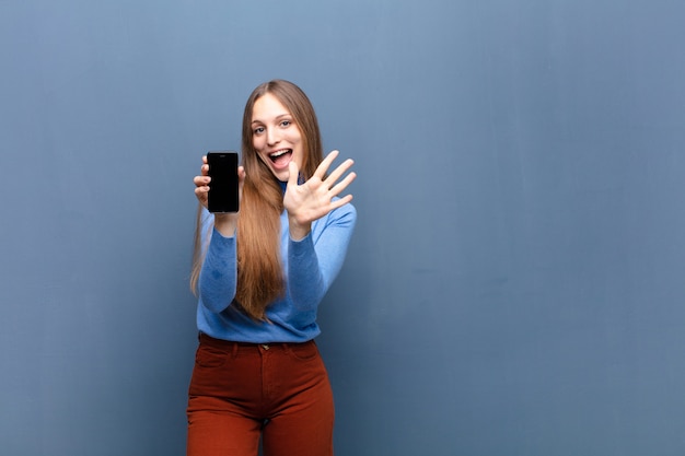 Young pretty woman using a smart phone  blue wall with a copyspace