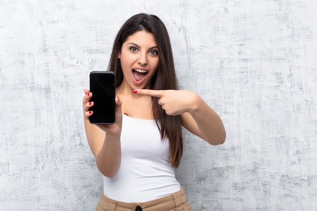 Young pretty woman using a smartphone against grunge wall