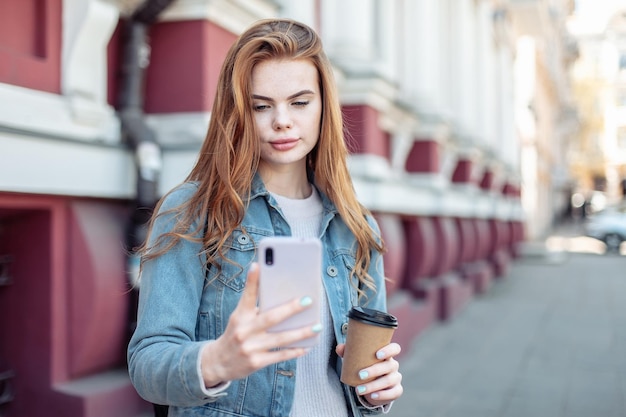 Young pretty woman using smartphone and holding a cup of coffee in the city