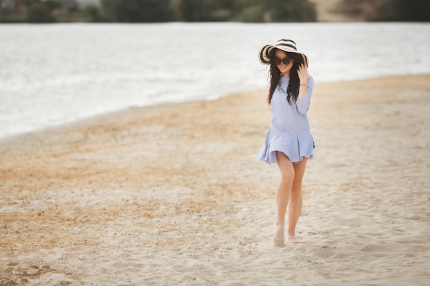 Young pretty woman walking on a beach. Attractive adult girl near the water relaxing. Beautiful woman on the sea