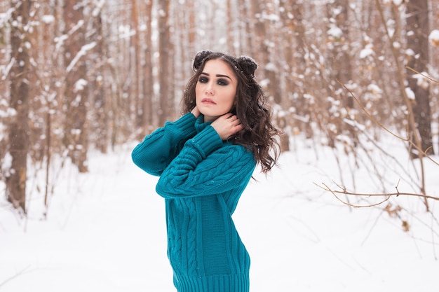 Young pretty woman walking in the winter snowy park at sunny day