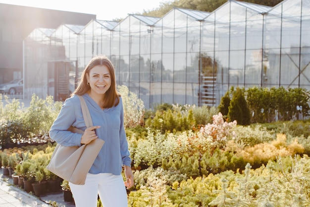 A young pretty woman walks down the street near the large greenhouses A woman goes to buy green plants for decoration Landscaping concept