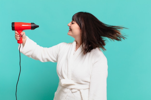 Young pretty woman wearing bathrobe happy expression and a hair dryer