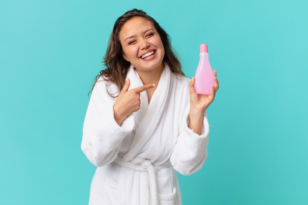 Young pretty woman wearing bathrobe and holding a clean product bottle