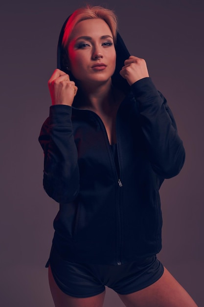 Young pretty woman wearing a black hood and shorts on dark background