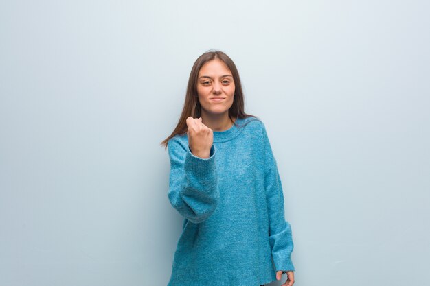 Young pretty woman wearing a blue sweater showing fist to front, angry expression